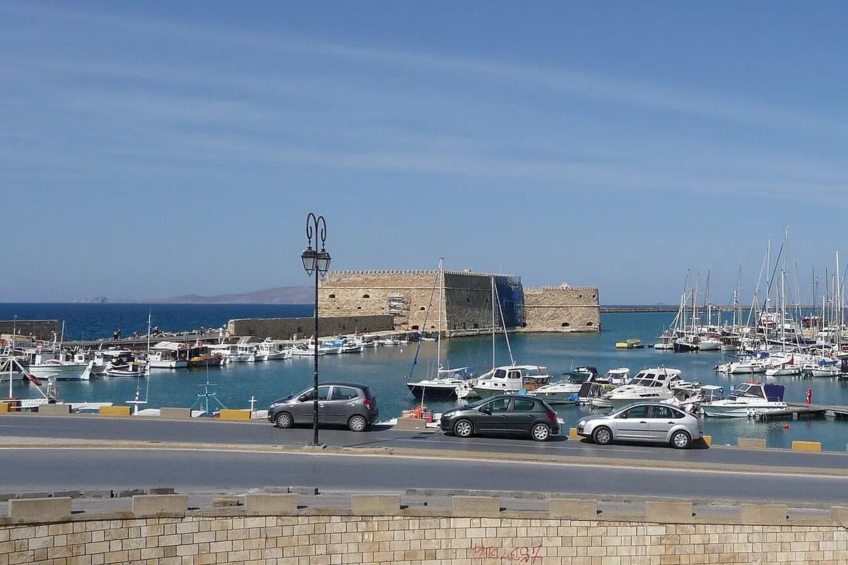 The Venetian sea fortress at the mouth of the old harbour in Heraklion, with moored boats and a seafront road in the foreground